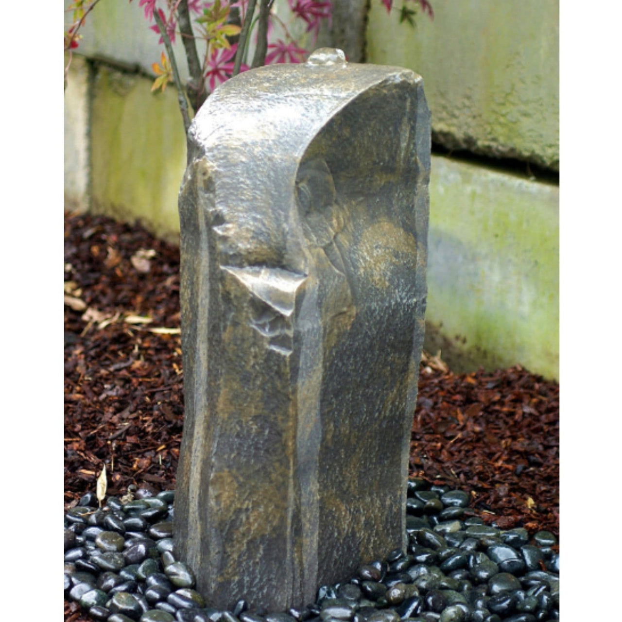 Outdoor Silver Rock Fountain With Yellow Wall And Pink Flowers Behind