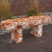 Red Onyx Garden Bench Near Brown Wall With Pebbles And Tall Grasses