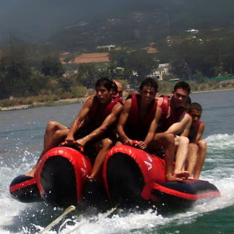 Red Shark 10 Person Banana Boat With Group Of Men Held On Tightly While Riding And Facing The Strong Waves