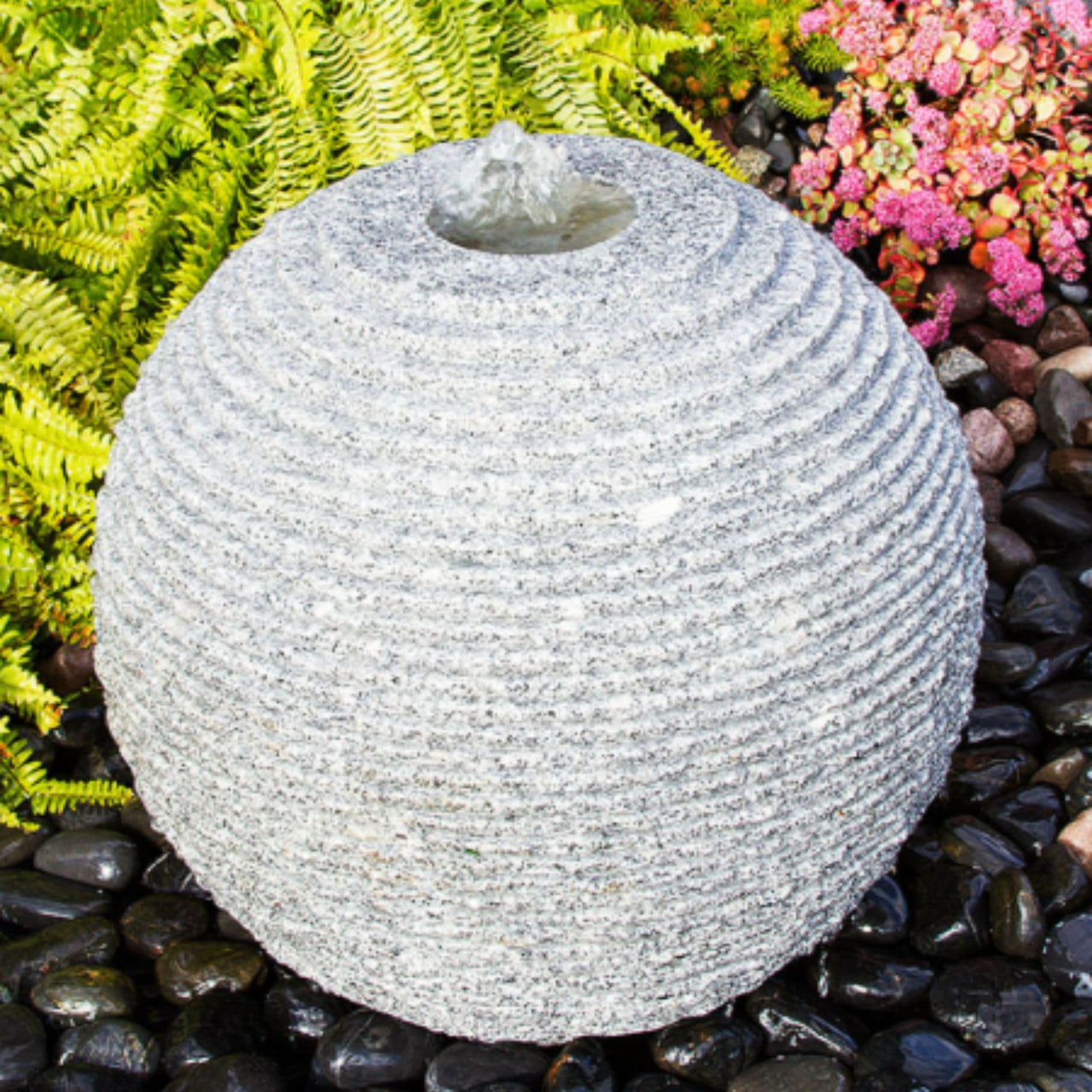 Ribbed Granite Stone Sphere Fountain With Ferns And Flowers Backdrop