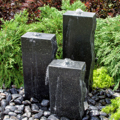 Rough Black Granite Triple Stone Fountain with 3 Smooth Sides With Shrubs And Red Leaves Plants Behind