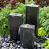 Thumbnail for Rough Black Granite Triple Stone Fountain with 3 Smooth Sides With Shrubs And Red Leaves Plants Behind