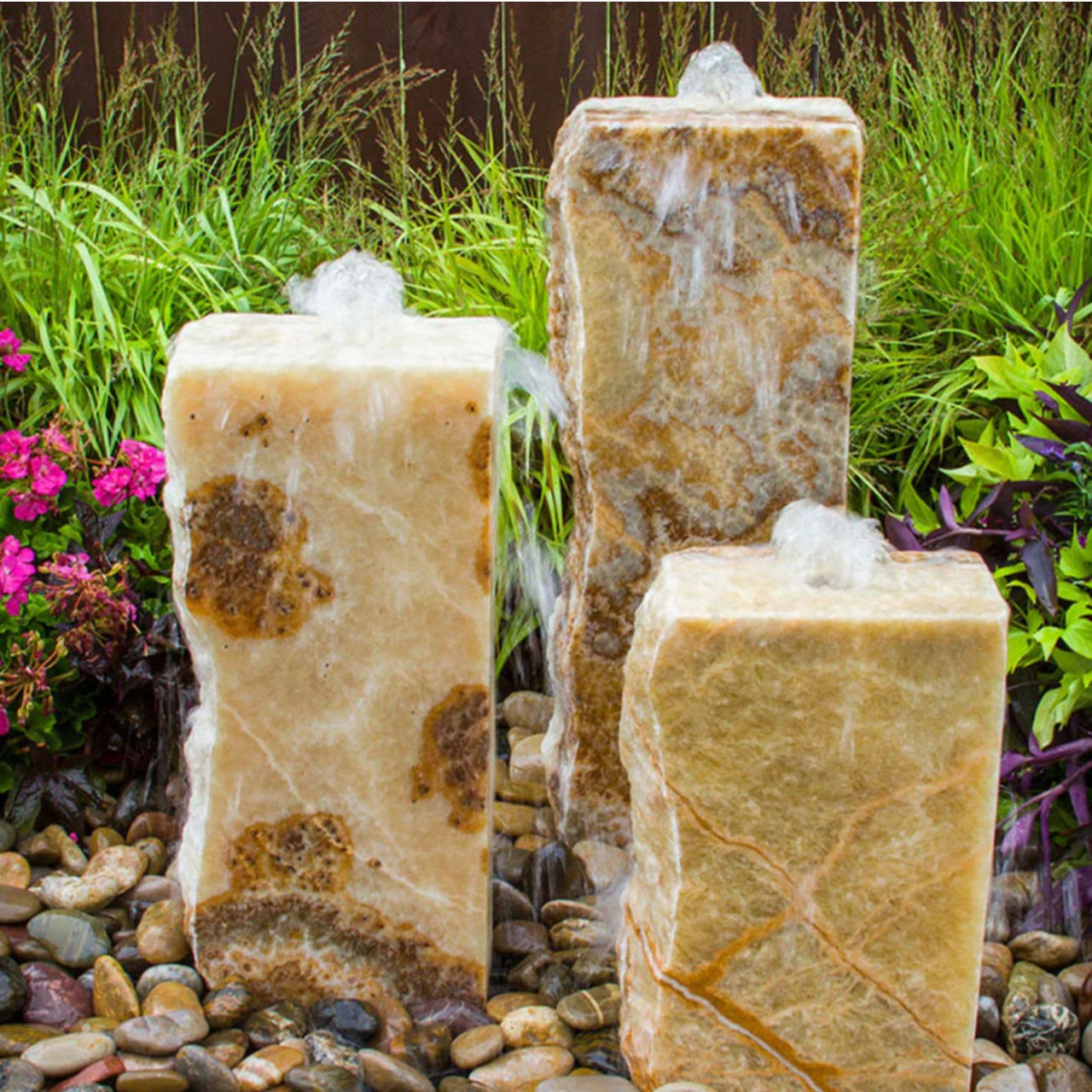 Rough Yellow Onyx Triple Stone Fountain with 3 Smooth Sides With Grasses, Plants And Pink Flowers  Behind