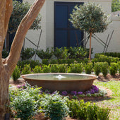 Rustic Outdoor Fountain On Cozy Landscape Surrounded By Small Tress And Plants