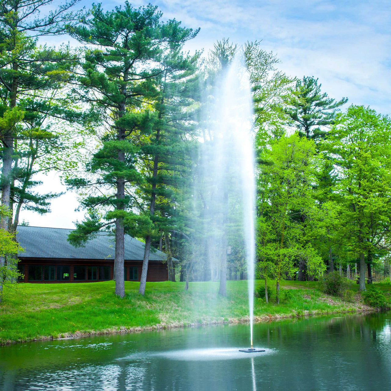 Scott Aerator Gusher Fountain On The Water With Green Trees In The Background