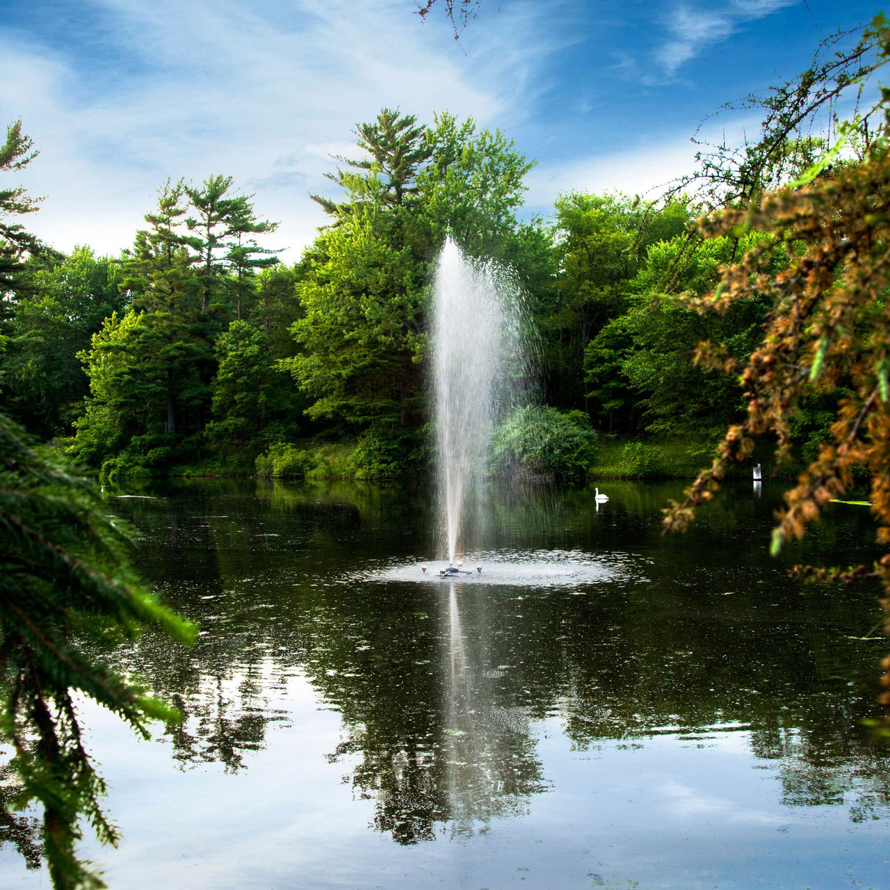 Scott Aerator Gusher Pond Fountain On The Water With Green Trees & A Blue Sky In The Background