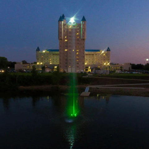 Scott Aerator Jet Stream Pond Fountain With Green Lights On The Water With A Building In The Background