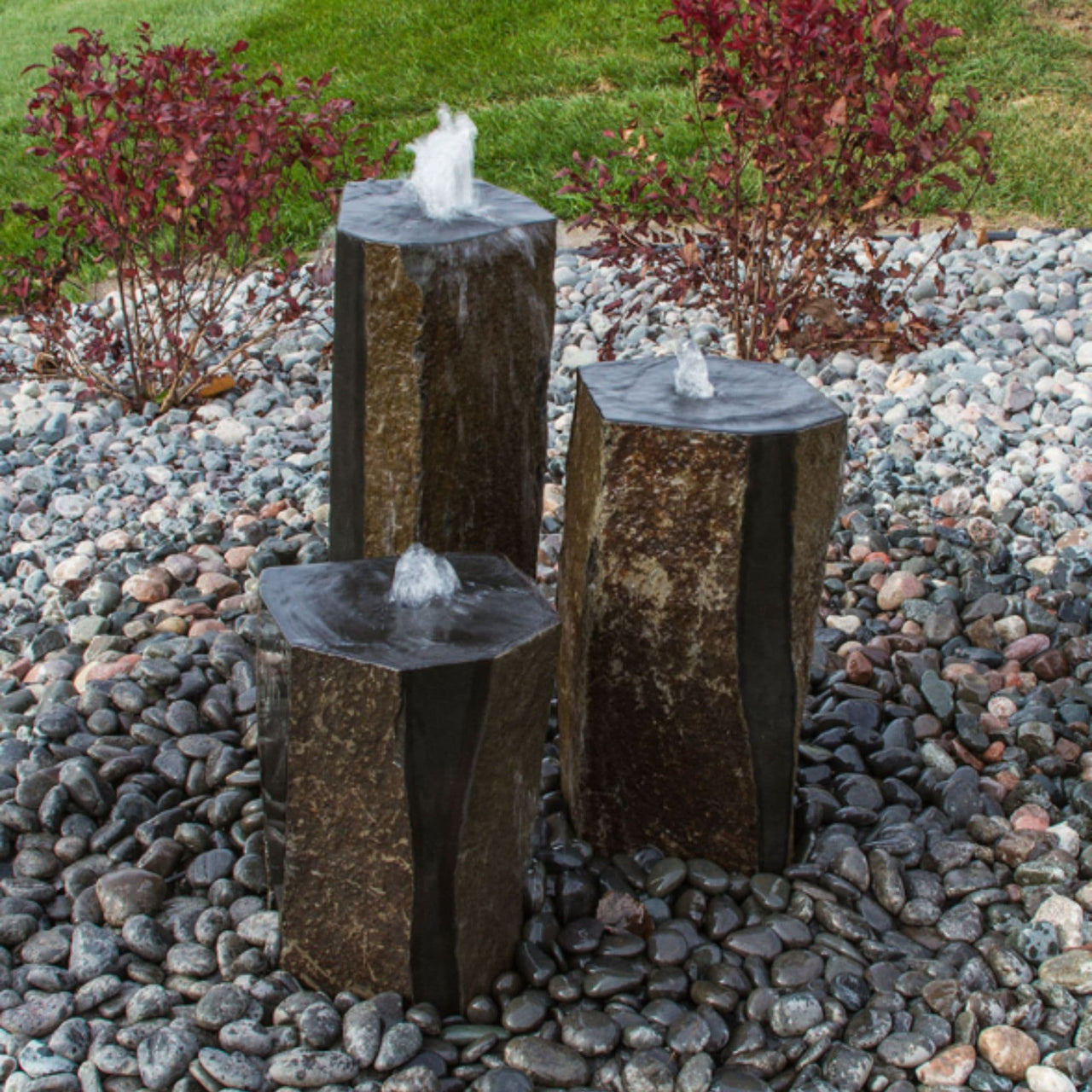 Semi-Polished Basalt Rock Column Fountain With Grassy And Shrubbery Background