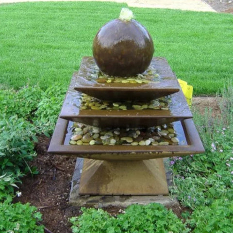 Shallow Three Tier Tapered Square Fountain With Green Plants And Plain Grass In The Background