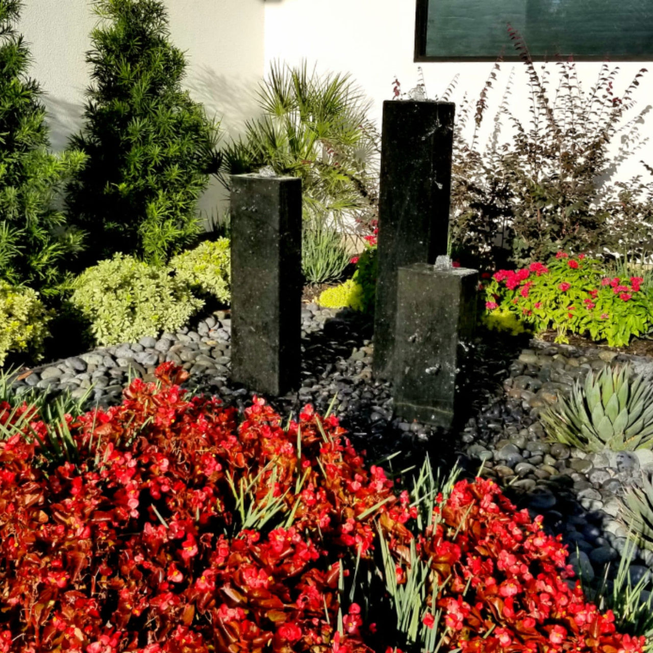 Smooth Black Granite Triple Stone Fountain Surrounded By Colorful Flowers And Greenery Plants