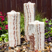 Smooth Red Onyx Triple Stone Fountain Surrounded By Colorful Plants And Flowers With Wooden Fence Background