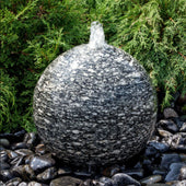 Speckled Granite Sphere Stone Fountain With Shrubs In The Background