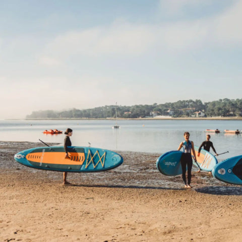 Spinera Lets Paddle 10.10 Paddle Board With Three People Carrying Boards by Shore