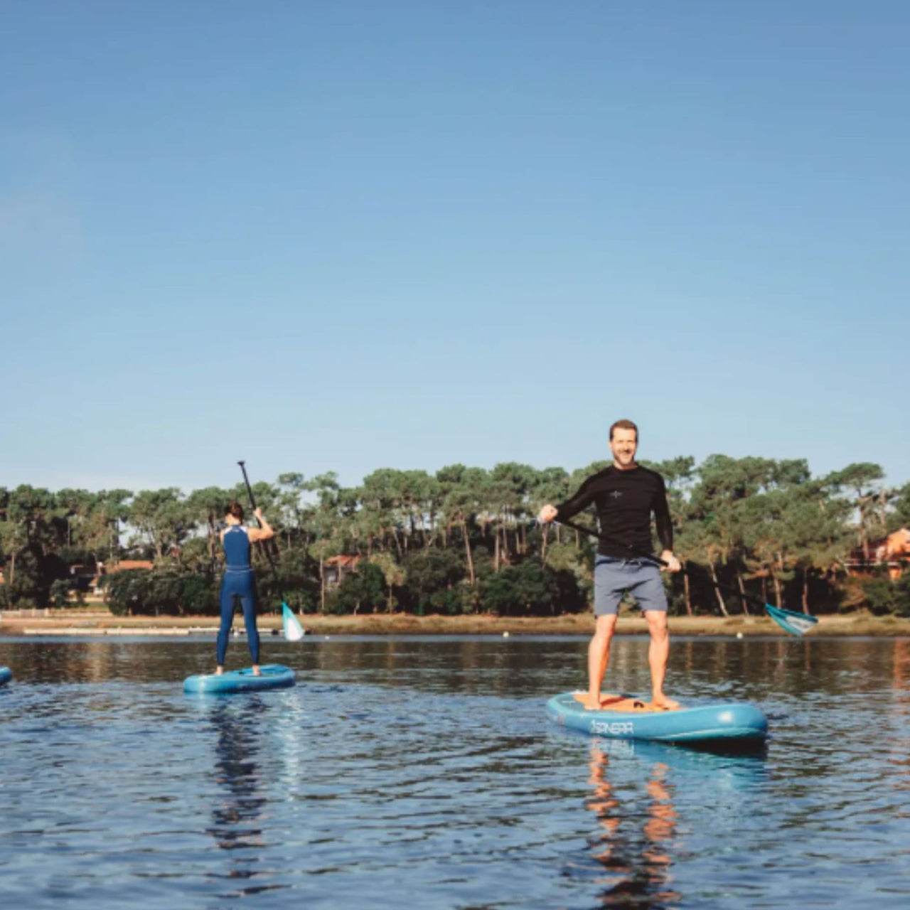 Spinera Lets Paddle 10.10 Paddle Board With Two Man and Woman Paddling Near Lake Shore