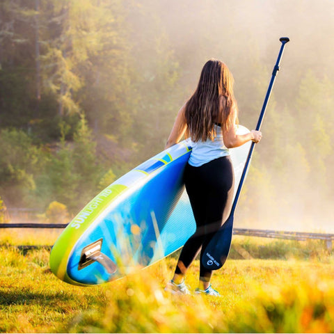 Spinera Sun Light 1.0 Paddle Board With A Woman Walking Carrying The Paddle and The Board