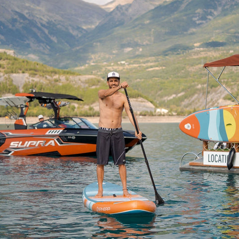 Spinera Supventure Sunrise 12 Paddle Board With a Man Paddling Next to a Boat with Mountain Background