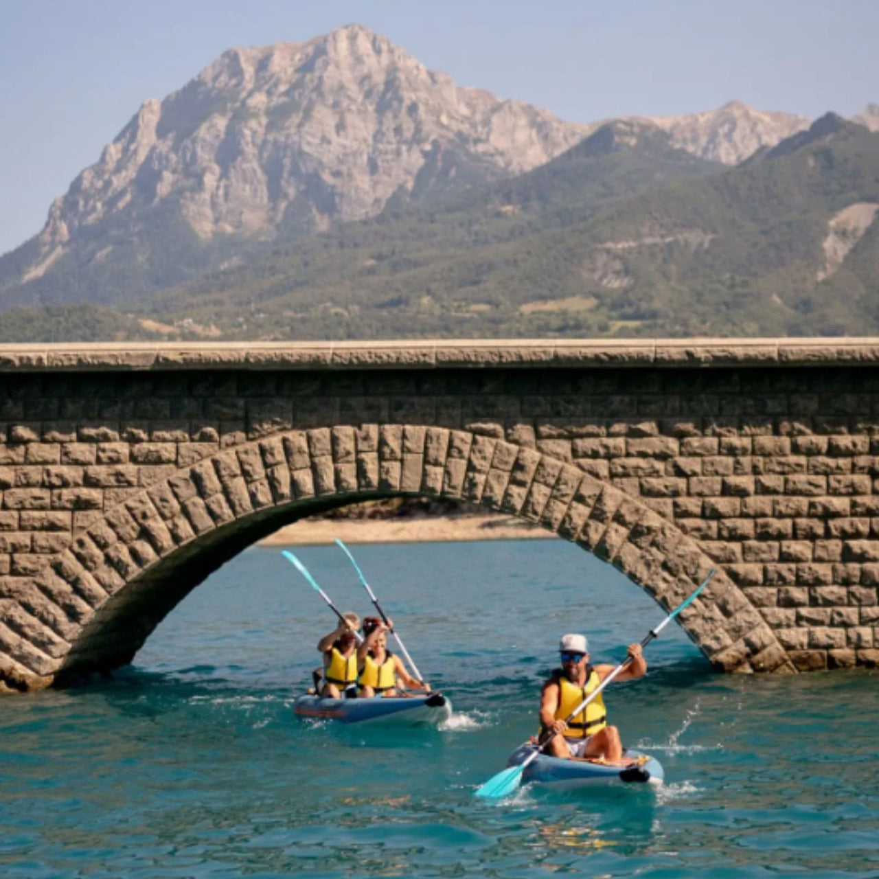 Spinera Tenaya 140 With Three People Kayaking Together On Blue Water With Stone Bridge Background