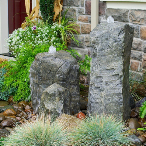 Stone Fountain with Accent Rock Surrounded By Plants With Brick Wall Background