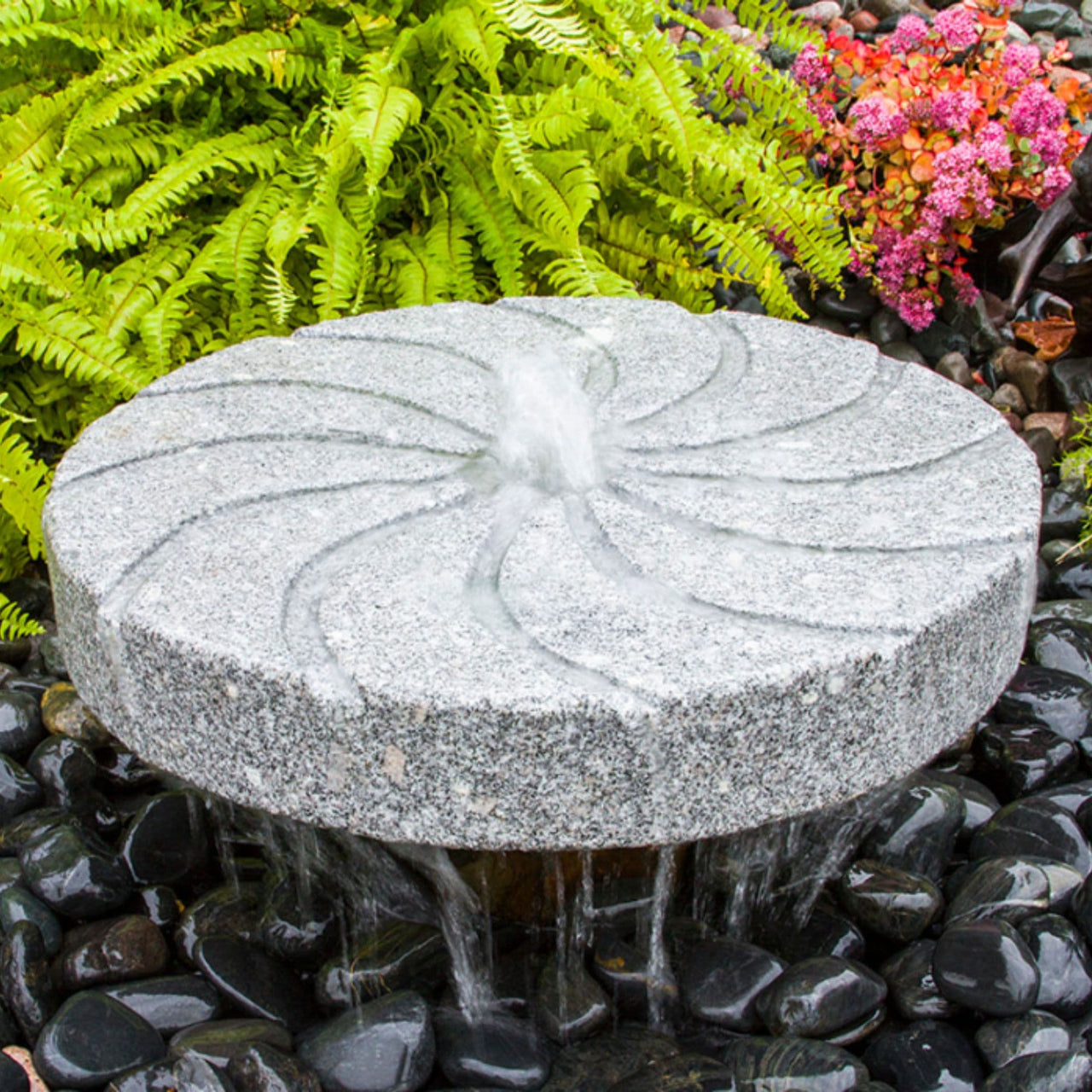 Swirl Millstone Granite Stone Fountain With Ferns And Flowers Behind