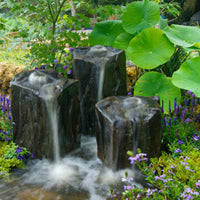 Thumbnail for Triple Column Outdoor Fountain Rocks Surrounded By Vibrant Purple Flowers With Large Leaves Background