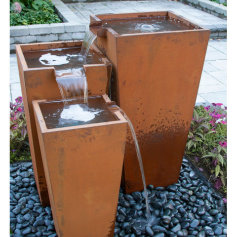 Triple Corten Steel Rusted Outdoor Fountain Surrounded By Pink Flowers With Stone Pavers Background