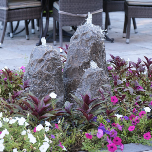 Triple Matterhorn Outdoor Fountain Rock Surrounded By Flowers With Chairs In The Back