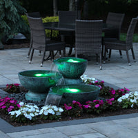 Thumbnail for Triple Spillway Stone Bowl Fountain Surrounded By White And Pink Flowers With Table And Chairs Background