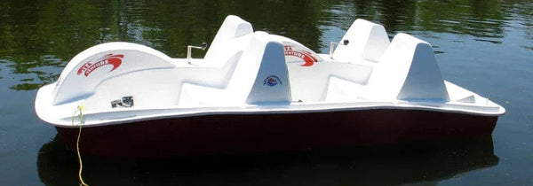 White SeaVenture pedal boat with a maroon hull moored on calm water, showing its rows of molded seats and pedal stations.