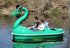 Green dragon-shaped pedal boat with a red-crested head, carrying three riders on a calm river