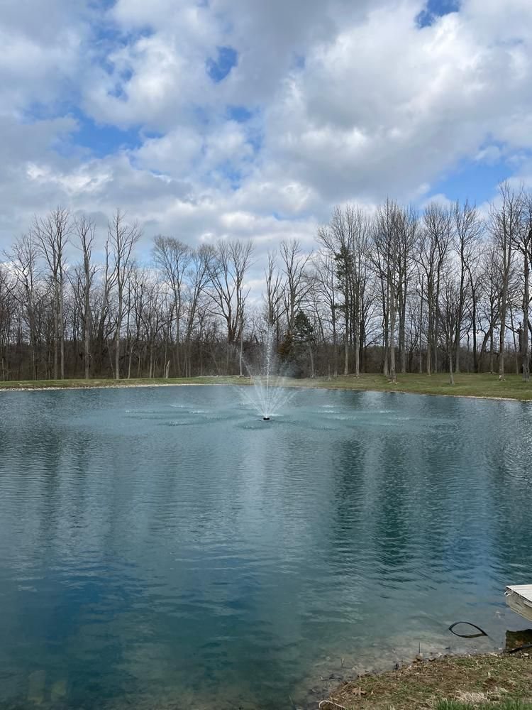 Fountain in a large still pond under a cloudy spring sky